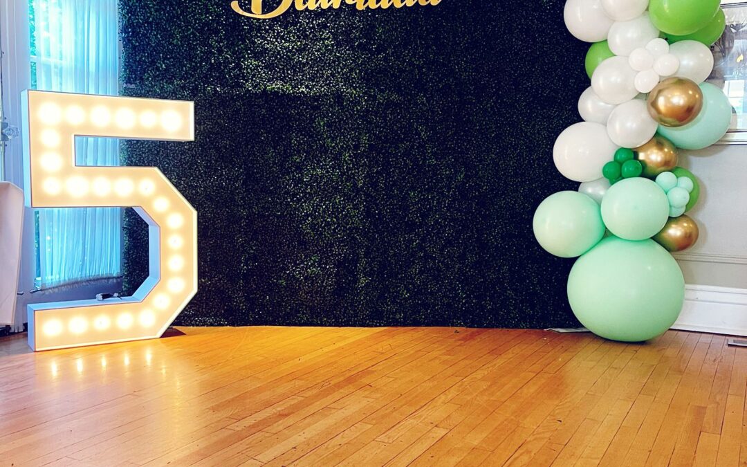 green boxwood wall with balloon decor and marquee number