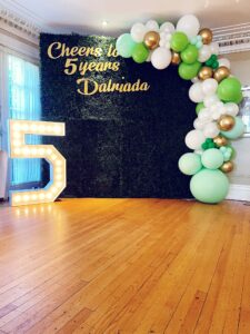 green boxwood wall with balloon decor and marquee number