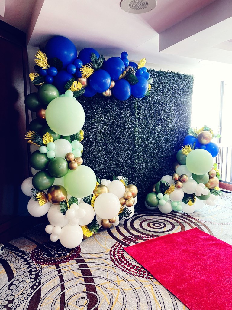green boxwood wall with balloon decor and red carpet